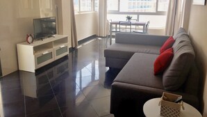 A modern living room with a flat-screen TV on a white stand, a grey sofa with red cushions, and a dining area with a table and chairs. - SUPER VIEWS IN SUIT. NEW WITH FREE WIFI / PETS PERMITTED!(4 people) (Benidorm)