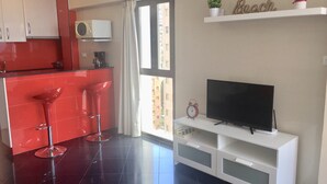 A modern kitchen with red cabinets, a white countertop, and a bar stool. There is a white entertainment unit with a flat-screen TV and a small table with a clock. - SUPER VIEWS IN SUIT. NEW WITH FREE WIFI / PETS PERMITTED!(4 people) (Benidorm)