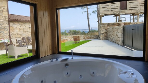 Un baño moderno con una bañera grande, una pared de piedra y vistas a un patio con mobiliario exterior.