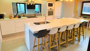Una cocina moderna con una isla central, taburetes de bar, horno empotrado y un ventanal grande.