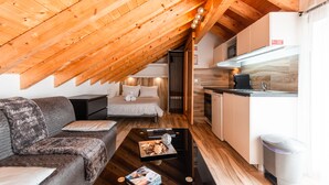 Um quarto de sótão acolhedor, com teto de madeira, um sofá, uma mesinha de cabeceira e uma pequena cozinha.