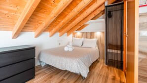Um quarto com teto inclinado, cama com colcha estampada, cômoda escura e piso de madeira.