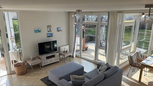 A spacious living room with a grey sofa, a flat-screen TV, and a dining area with a table and chairs. - Haffnest with wonderful views of the Salzhaff  (Rerik)