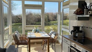 A modern kitchen with large windows, a dining area with a table and chairs, and a grey sofa. - Haffnest with wonderful views of the Salzhaff  (Rerik)