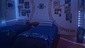 Een kamer met twee bedden, led-strips langs de muren en diverse ingelijste foto's aan de wand.