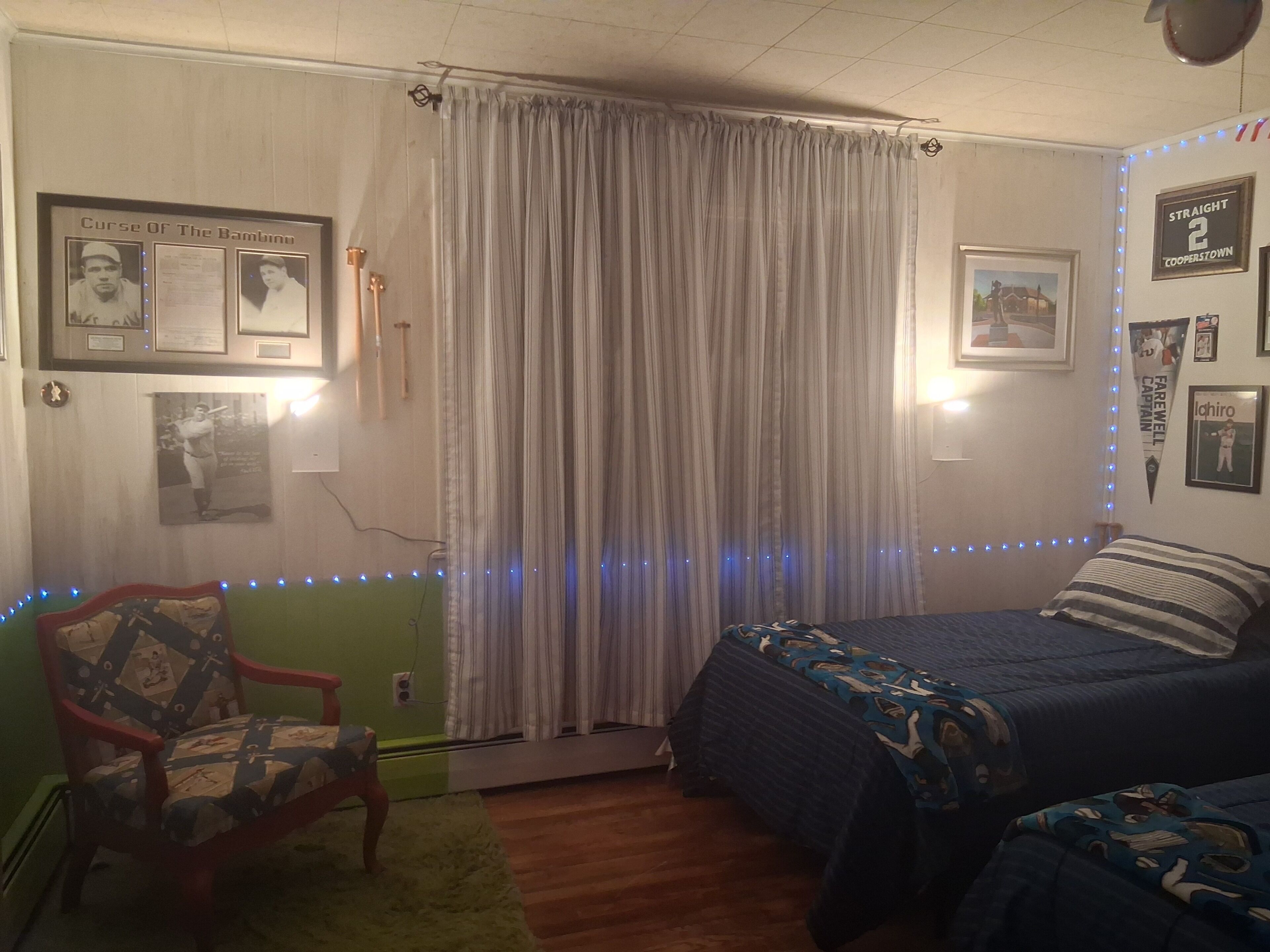 Un dormitorio con cama, una silla, una cortina y adornos en la pared.
