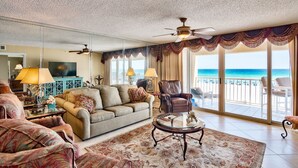 Ein geräumiges Wohnzimmer mit großem Fenster zum Strandblick, ausgestattet mit einer Couch, Sesseln und einem Couchtisch.