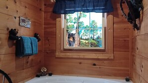 Ein Zimmer in einer Holzhütte mit Fenster, einer Badewanne und einer kleinen Eule als Dekoration.