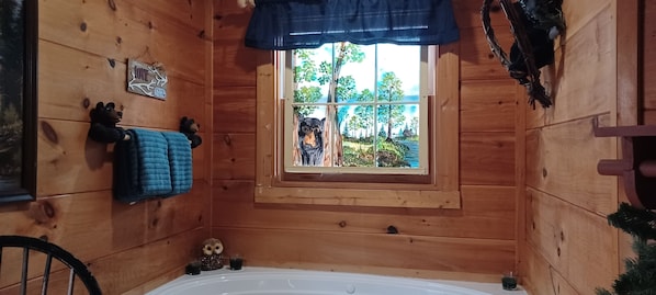Une pièce de cabane en bois avec une fenêtre, une baignoire et une petite décoration représentant un hibou.