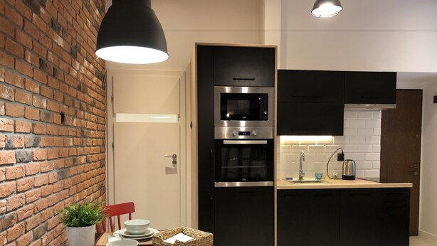 Een kleine keuken met een bakstenen muur, moderne apparatuur en een eethoek met een tafel gedekt voor twee personen.