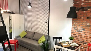 Een moderne woonkamer met een grijze bank, rode en zwarte stoelen, een eettafel en een bakstenen muur.