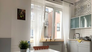 Een moderne keuken met witte kasten, een eettafel en een raam met lichte gordijnen.