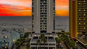 A tall hotel with multiple floors, a central courtyard, and a view of the ocean at sunset. - 22nd Floor Beachfront Suite - Amazing Views (Gulf Shores)