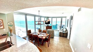 A spacious living area with a large window overlooking the beach, a dining area with a wooden table and chairs, and a cozy seating area with a sofa and armchairs. - 22nd Floor Beachfront Suite - Amazing Views (Gulf Shores)