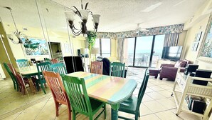 A dining area with a large table and chairs, a chandelier, and a television in the background.
