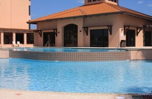 A swimming pool with a tiled edge, adjacent to a building with a tiled roof and large windows. - SeaChase 602 East (Orange Beach)