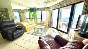 A living room with a brown leather sofa, a yellow sofa, a glass coffee table, and a ceiling fan.