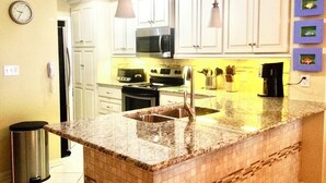 A kitchen with white cabinets, a granite countertop, a stainless steel sink, a microwave, and a coffee maker.
