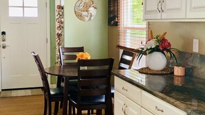 A dining area with a wooden table and chairs, a vase with flowers, and a kitchen counter with cabinets. - Quaint and Charming 2 bd, 1 bath,  Central Location, easily accessible! (San Diego)