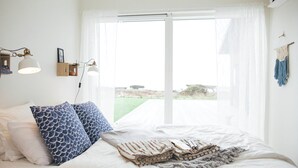 A bedroom with a bed, pillows, a bedside lamp, a window with curtains, and a view of the outdoors. - Johanna's Hotel (Bua)