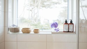 A bathroom with a window, a sink, and toiletries on the windowsill. - Johanna's Hotel (Bua)