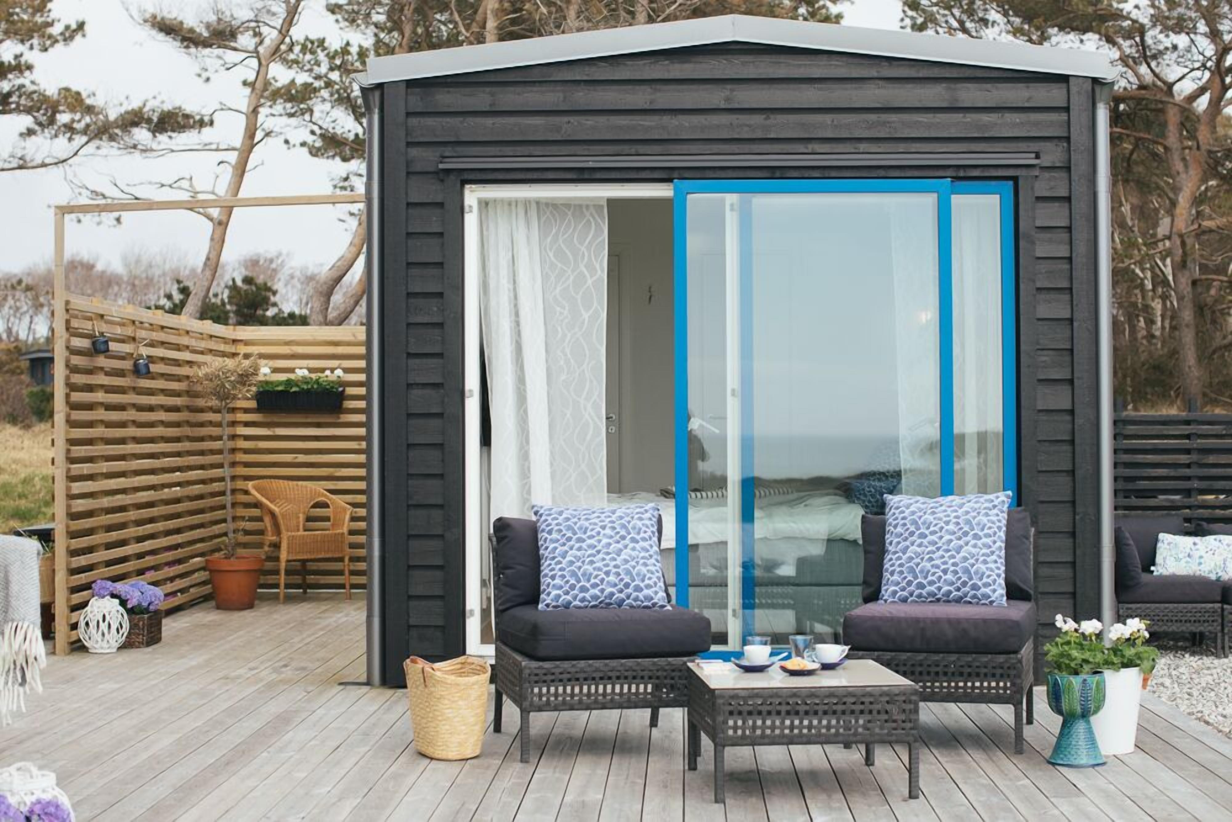 Ett trädäck med en svart pergola, två bekväma sittgrupper och ett bord med en kopp och ett fat.