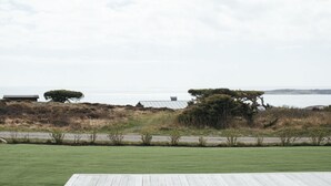 A grassy area with a wooden deck, a large tree, and a building in the background. - Johanna's Hotel (Bua)