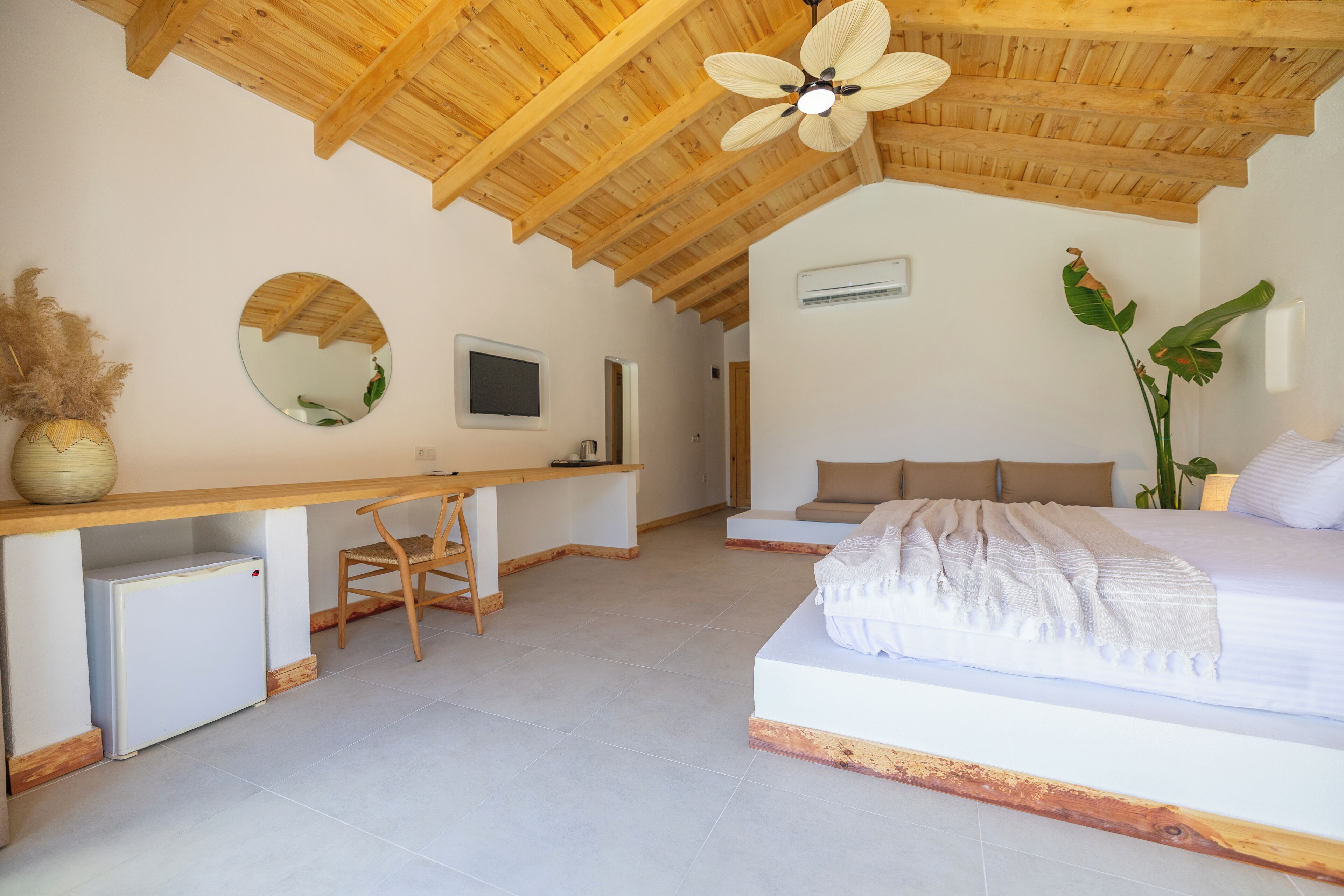 A bedroom with a wooden ceiling, a bed, a desk, a chair, and a television.