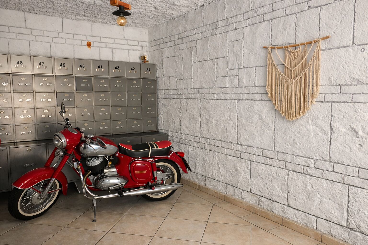 A motorcycle in a room with lockers and a macrame wall hanging.