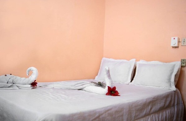 A hotel room with a bed, white bedding, and a wall-mounted electrical outlet.