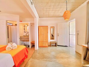 A hotel room with a bed, a bathroom, a wooden wardrobe, a mirror, and a hanging light fixture. - Outsite Todos Santos – Formerly Perro Surfero Hotel Boutique (Todos Santos)
