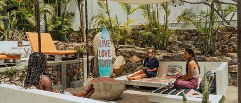 A tropical outdoor seating area with lounge chairs, a stone wall, and a surfboard sign.