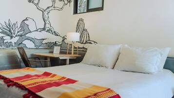 A hotel room with a bed, a nightstand, a lamp, and a wall mural.