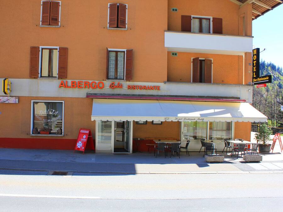 A hotel named "Albergo Bistrotante" with a restaurant sign, outdoor seating, and a mountain view.