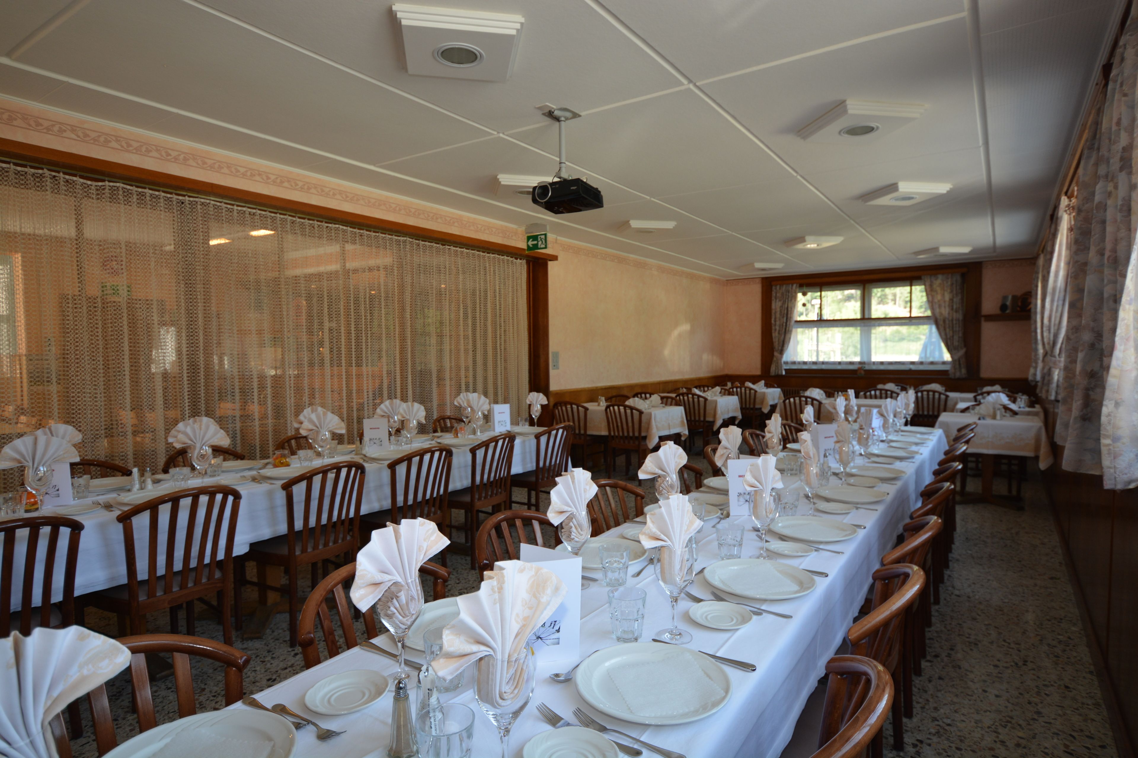Un salón de banquetes con largas mesas dispuestas para un evento formal, equipado con sillas, mesas y un proyector.