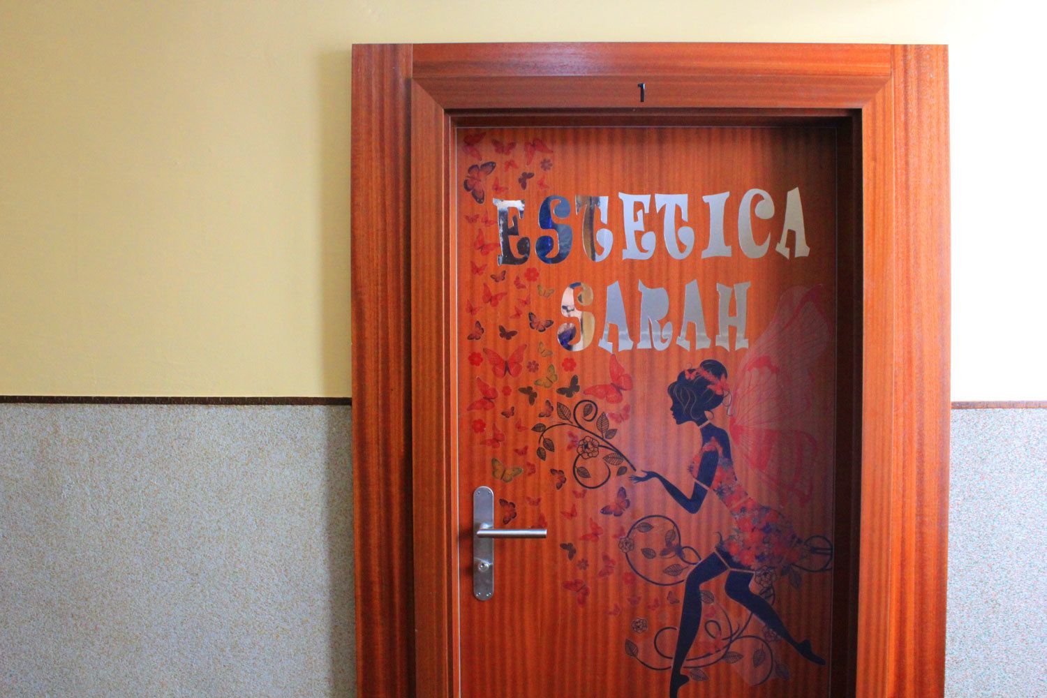 Una puerta de madera con el nombre "ESLETICA SARAH" y la silueta de una mujer con alas de mariposa.