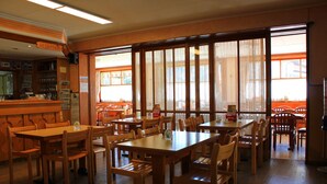 A restaurant with wooden tables and chairs, a reception area, and large windows with lace curtains. - Albergo Ristorante Baldi (Prato)