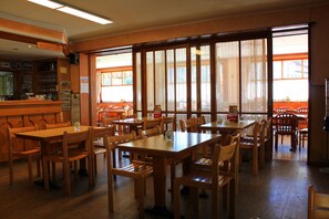 A restaurant with wooden tables and chairs, a reception area, and large windows with lace curtains. - Albergo Ristorante Baldi (Prato)