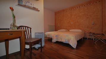 A bedroom with a wooden floor, a bed with a patterned bedspread, a chair, a small table, and a radiator.