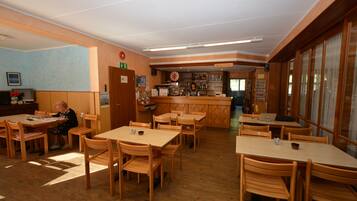 A restaurant with wooden tables and chairs, a reception desk, and a bar area.