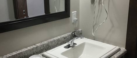 A bathroom with a white sink, a mirror, and a hairdryer mounted on the wall.