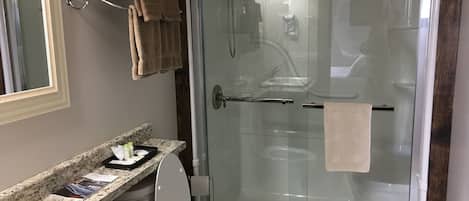 A bathroom with a glass-enclosed shower, a toilet, a sink with a marble countertop, and a towel rack with folded towels.