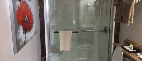A glass-enclosed shower with a white toilet and a towel rack.