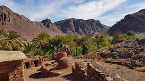 An ancient ruin with stone structures and palm trees in a mountainous landscape.