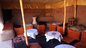 A traditional room with a thatched roof, multiple cushions, and small tables covered with white cloths.