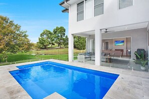 A modern house with a swimming pool, a covered outdoor seating area, and a view of a green landscape.