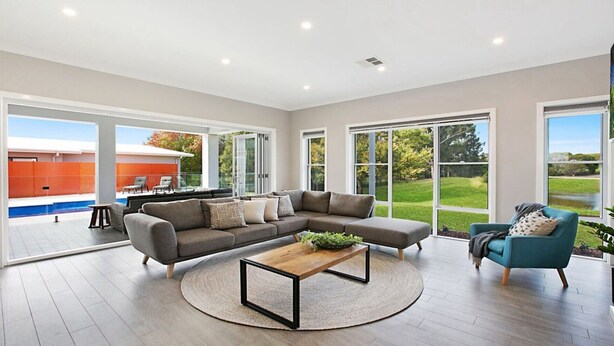 Un salon spacieux avec un grand canapé d’angle, une table basse et une vue sur une piscine et un espace extérieur, le tout visible à travers de grandes fenêtres.