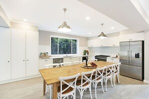 A modern kitchen with white cabinetry, a wooden dining table, and a stainless steel refrigerator.