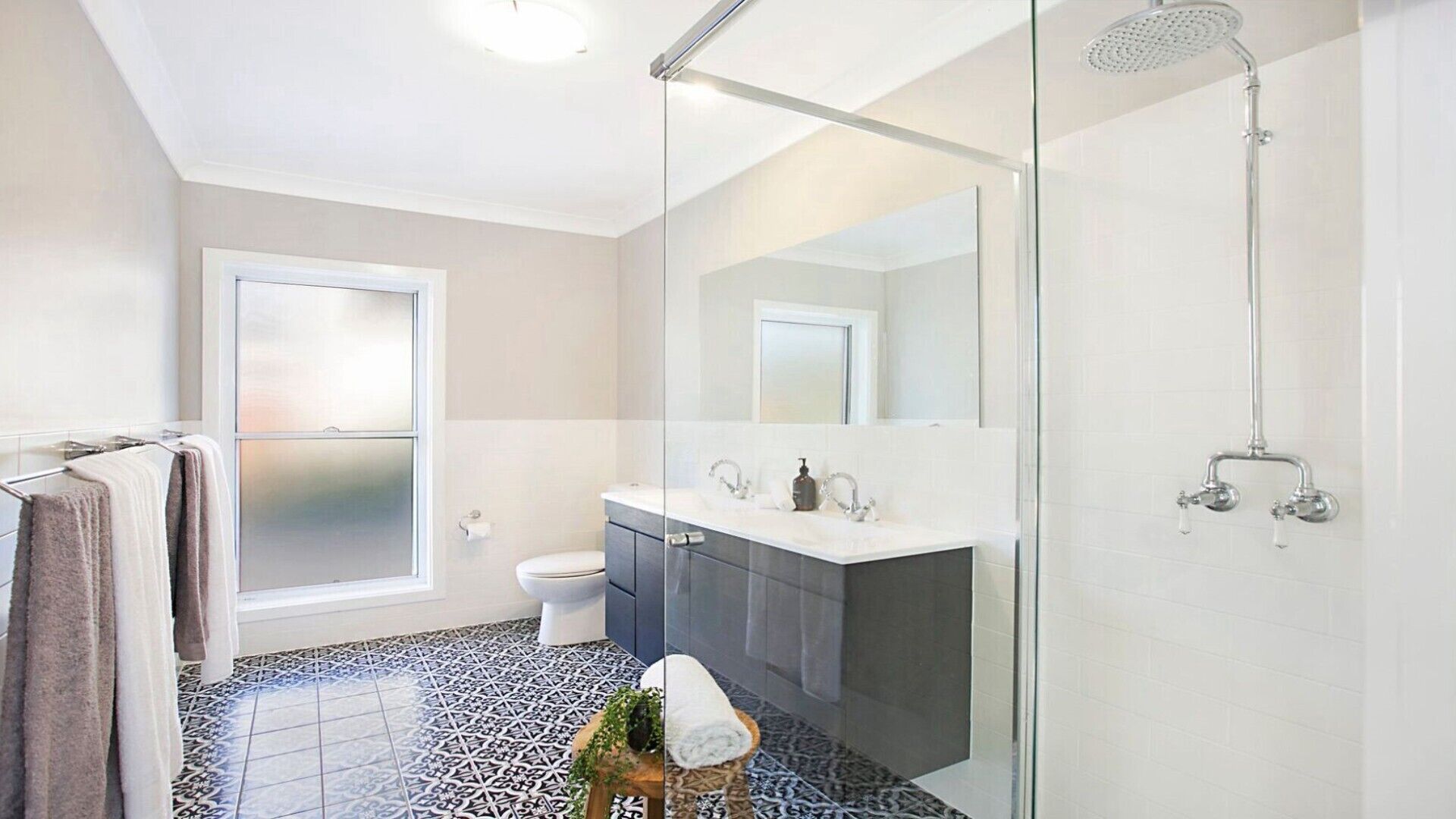 Een moderne badkamer met een glazen douchecabine, een wit toilet en een donker badmeubel met spiegel.
