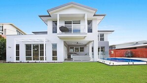Une maison moderne à deux étages, dotée d’un balcon, d’une piscine et d’une pelouse bien entretenue.